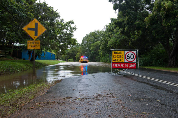 Queensland Flooded Road after tropical Cyclone Marcia Palmwoods, Australia - February 21, 2015: Image shows a flooded road with road closed ahead roadsign. Yellow rural firebrigade four wheel drive vehicle crossing the floodwater. Palmwoods, Sunshine Coast, Queensland, Australia queensland floods stock pictures, royalty-free photos & images