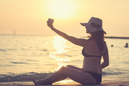 Woman taking a photo of herself on tropical beach at sunset