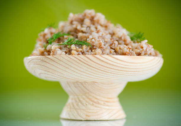 Boiled buckwheat in a wooden bowl on a green background