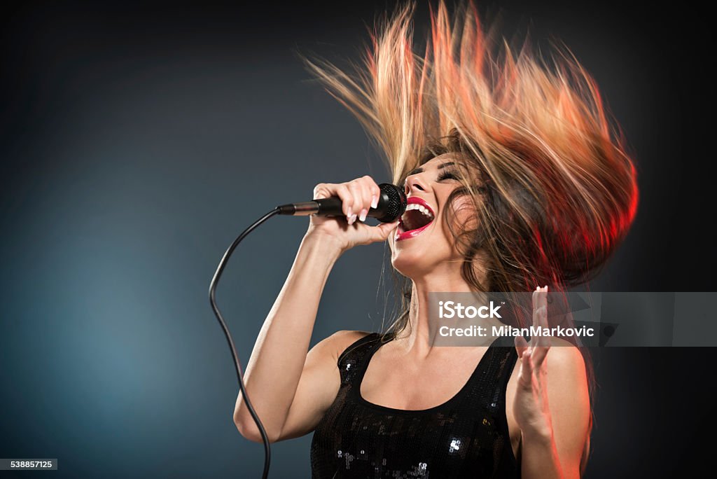 Cute Rock Star A young woman rock singer with tousled long hair holding a microphone with stand and sing with a wide open mouth. Stage - Performance Space Stock Photo