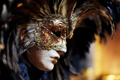 Young Woman dressed in beautiful elaborate costume wearing red mask, posing for the Carnival of Venice, by the Bridge of Sighs, one of the iconic sights of the city - Venice, Italy