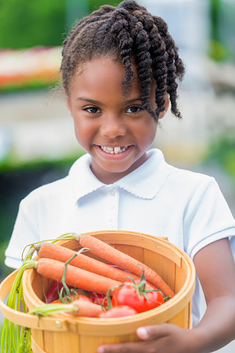 Happy african american girl at farmers market with fresh vegetables.