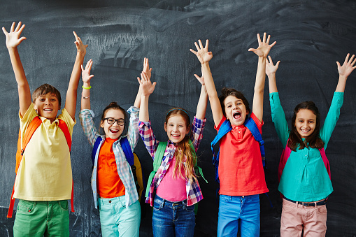 Excited schoolchildren standing with hands up