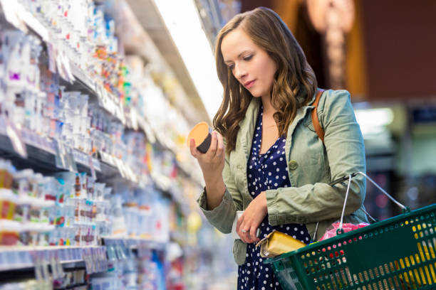 Woman reading food labels at grocery store Woman at grocery store reading food labels while holding her shopping basket. nutrition label stock pictures, royalty-free photos & images