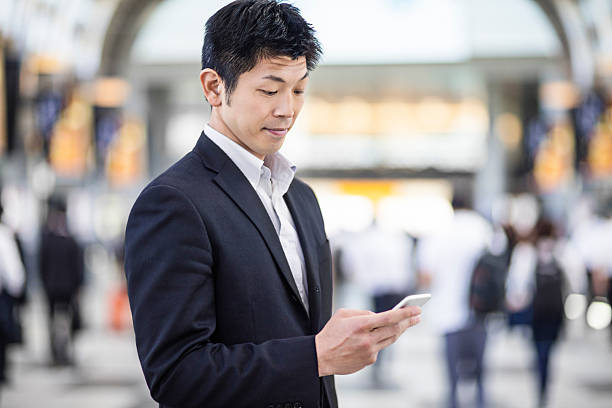 homem de negócios japoneses a olhar para o seu telefone no posto de trabalho - rush hour commuter on the phone tokyo prefecture imagens e fotografias de stock