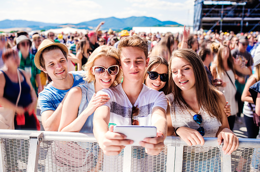 Teenagers at summer music festival in crowd taking selfie with smartphone, enjoying themselves
