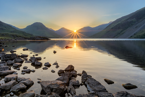 Golden sunrise at Wastwater lake with rocks and mountains.