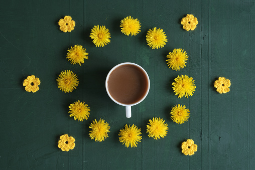 Cup of coffee, dandelions and crocheted flowers on green background.