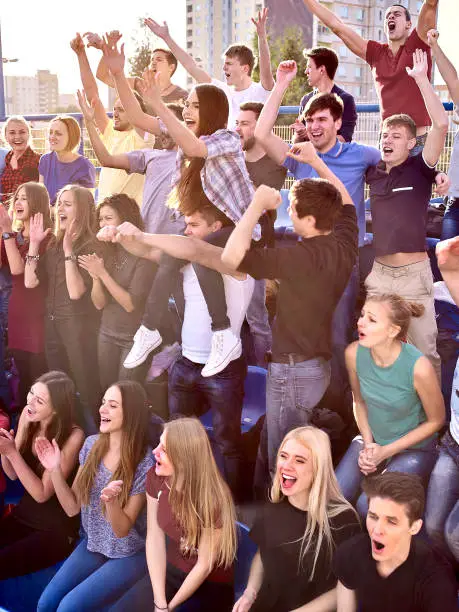 Photo of Sport fans hands up and singing on tribunes.