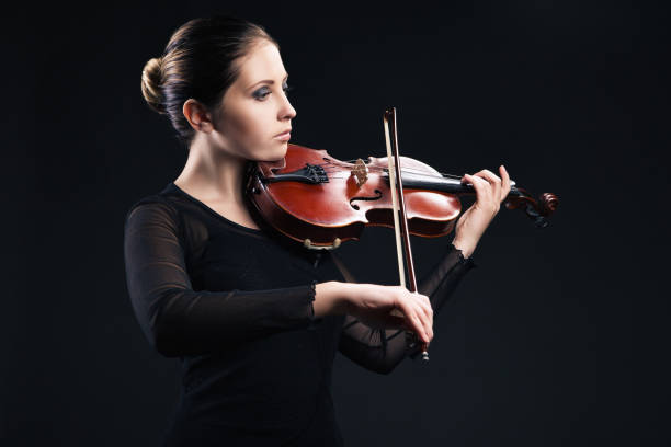 istock Beautiful young woman playing violin over black 538891566