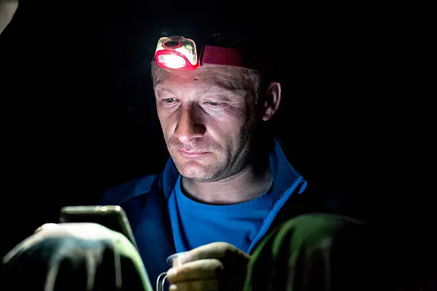 camping outdoors in nature on open sky at night , explorer is texting and using phone