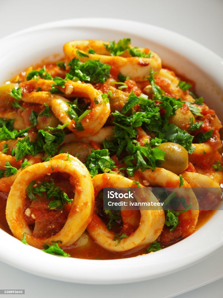 Stewed squid (calamari) Calamari stewed in tomato and onion sauces with olives, topped with parsley. Vertical shot Calamari Stock Photo