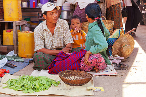Heho, Myanmar - March 02, 2011 - Young Burmese man selling food with his family at five-day market while sitting on the ground