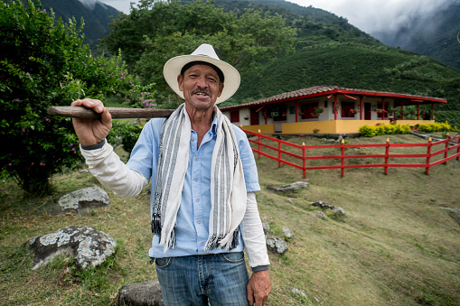 Colombian farmer looking very happy working at a farm with a house at the background