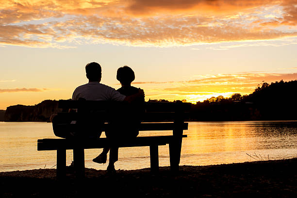 カップル、美しい夕日を眺めて - bench ストックフォトと画像