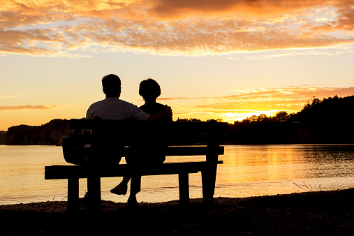 The Silhouette of a couple watching a beautiful sunset together while sitting on a bench