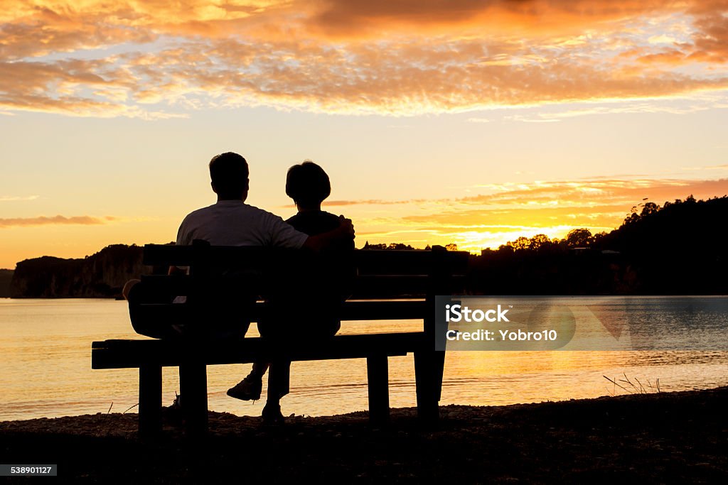 Couple watching a beautiful sunset together The Silhouette of a couple watching a beautiful sunset together while sitting on a bench Couple - Relationship Stock Photo