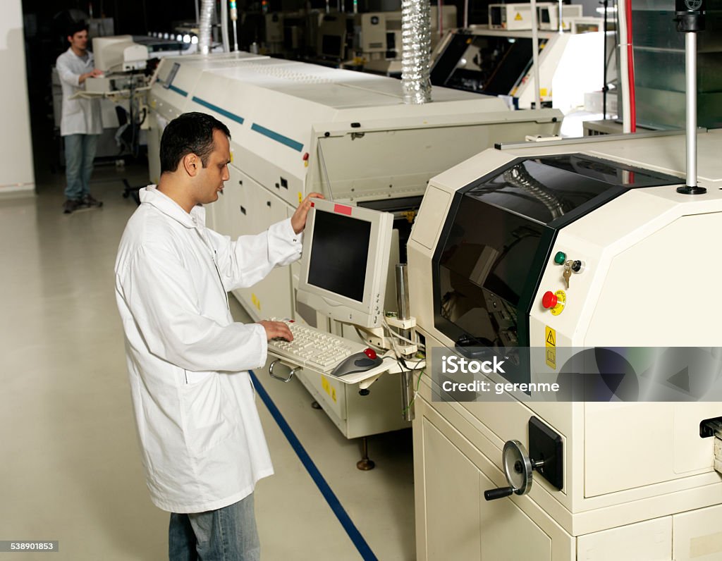 Operators using a tech machine in a factory Technician looking at camera and operating a computerized machinery in a factory 2015 Stock Photo