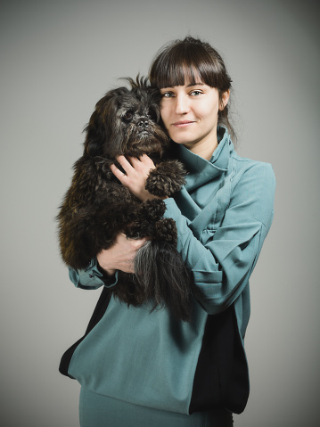 Studio portrait of a caucasian young woman looking at camera posing with her dog. The woman has around 25 years and has long hair and casual clothes. Vertical color image from a DSLR. Sharp focus on eyes.