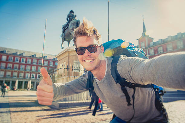 young attractive student backpacker tourist taking selfie photo with stick and mobile phone outdoors enjoying holidays travel destination in tourism and exploring concept