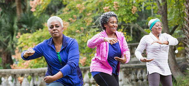 Three senior black women practicing Tai Chi Three senior African American women at the park doing Tai Chi exercises.  Focus is on the women wearing pink and blue. exercise class photos stock pictures, royalty-free photos & images