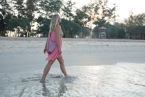 Woman walk along beach, in sea shallows, at sunrise
