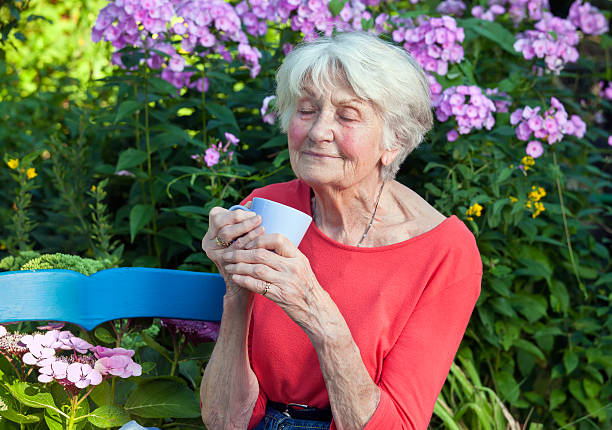 задумчивый старая женщина с кофе в саду. - senior women senior adult bench flower стоковые фото и изображения