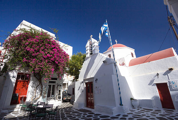 Mykonos Town, Greece - August 30, 2014: Tiny town square in Mykonos Town with vehicles passing through and shop names visible.