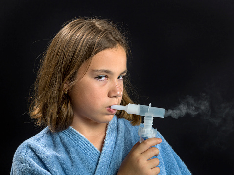 Caucasian little girl using a respiratory device also called inhaler on black background (this picture has been shot with a super high definition Hasselblad HD3 II 31 megapixels camera)