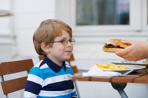 Cute little boy eating fast food: french fries and hamburger in cafe