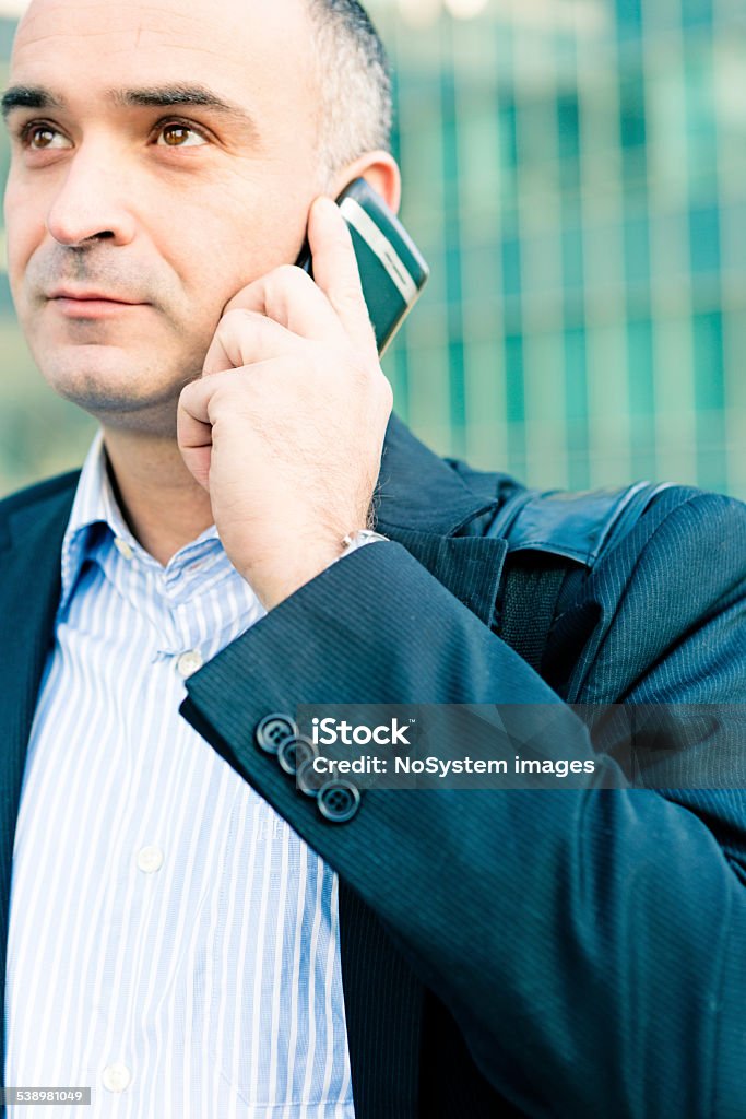 Businessman on a Cellphone Handsome businessman holds a mobile phone to his ear while outside the office. Vertical shot.Canon 5D MK III 2015 Stock Photo