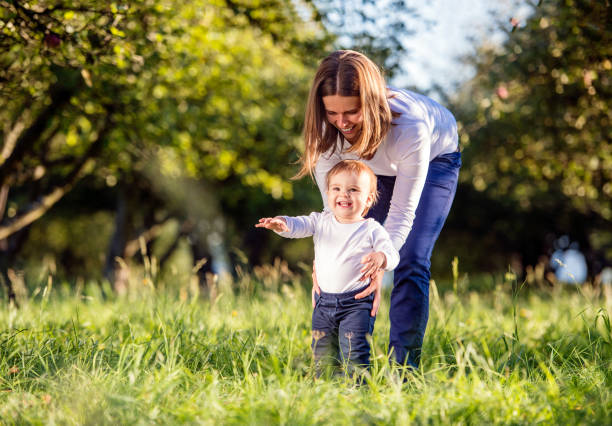 Mother holding her son making first steps, green nature