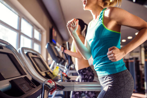 Two fit women running on treadmills in modern gym Two attractive fit women running in sports clothes on treadmills in modern gym blonde female bodybuilders stock pictures, royalty-free photos & images