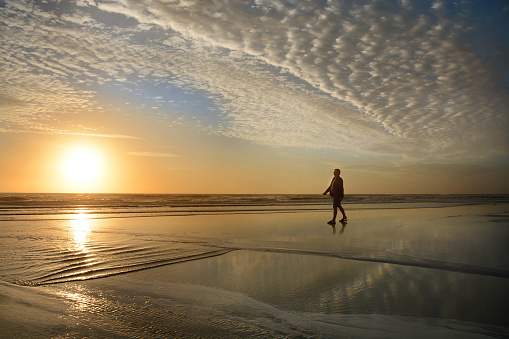Man walking and relaxing on the beach at sunrise. Beautiful cloudy sky reflected on the beach. Jacksonville, Florida, USA.