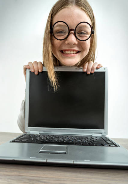 Smiling schoolgirl peeking from behind the laptop. Photo of teen school girl wearing glasses, creative concept with Back to school theme