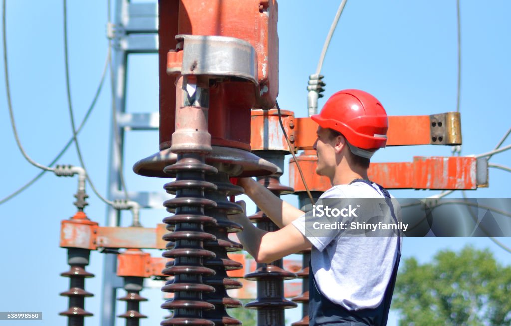 Mechanic Works at the Power Plant Repairman working at the power substation. Men wearing protective workwear and red hardhat. Men Stock Photo