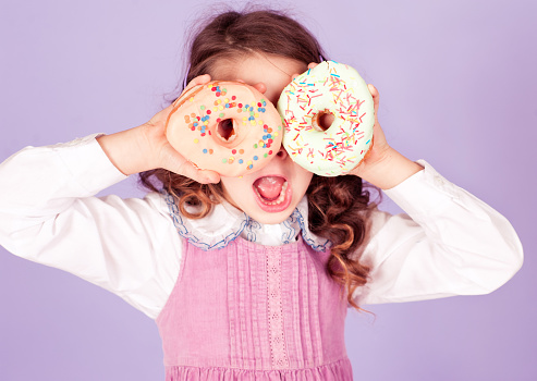 Cute kid girl 4-5 year old holding two tasty donuts in room. Having fun.