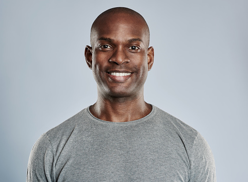 Single handsome black man with shaved head and pleasant smile in gray compression shirt over neutral background