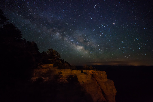 The silhouette of an adult man standing looking up at the sky while watching the milky way. He was on a night walk near Torre de Pedra, in a rural region of Ribeirão Claro, Paraná State, Brazil. The impression one has is that the stars come out of the Stone Tower, as if stars come out of a chimney.