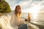 Cheerful young woman enjoys a drink by the lake shore