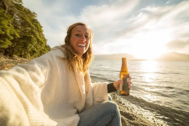 Photo of Cheerful young woman enjoys a drink by the lake shore