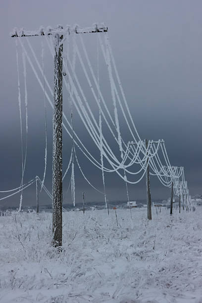 Broken phase electrical power lines with hoarfrost on the wooden electric poles on countryside in the winter,  pole with wires after storm