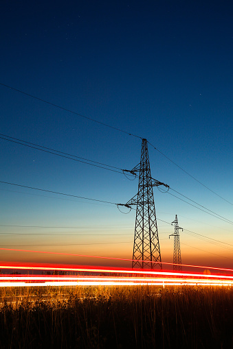 Pylons and electricity powerlines at night with traffic lights in front