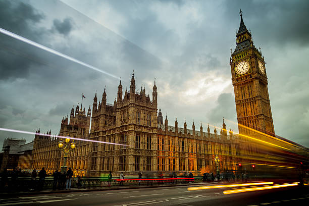 Houses of Parliament Big Ben and the Houses of Parliament in London, England. The building is lit up and set against a dramatic sky with cars and busses zooming by on Waterloo Bridge. houses of parliament london stock pictures, royalty-free photos & images