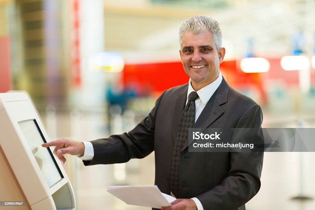 mature businessman using self help check in machine happy mature businessman using self help check in machine at airport. 2015 Stock Photo