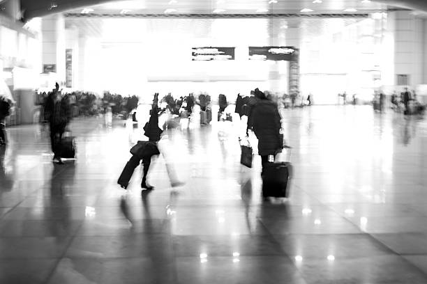 Woman traveler with travel suitcase luggage walking in airport terminal hall walkway for vacation business concept vacationing travel. Black and white picture