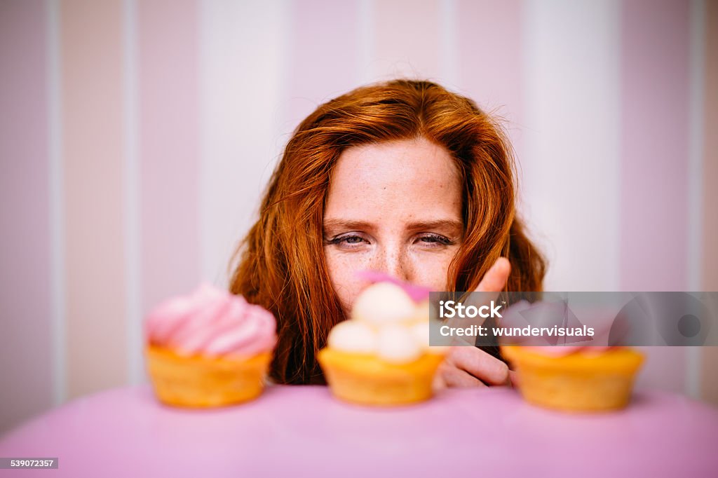 Young Woman Really Wants To Eat Cupcakes Young red head woman really wants to eat pink cupcakes Women Stock Photo