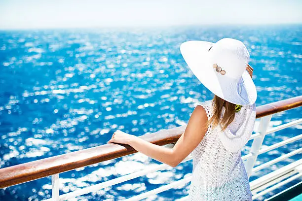 Unrecognizable woman with hat on a cruise ship looking at the view.