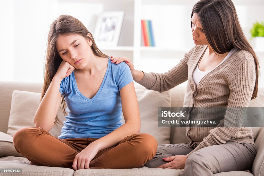 Mother and daughter Mother and teen daughter after quarrel on sofa at home.Problems between generations concept. Teen closed his ears with his hands while her mom yells at her.Problems between generations concept. Teen closed his ears with his hands while her mom yells at her. Adolescence Stock Photo