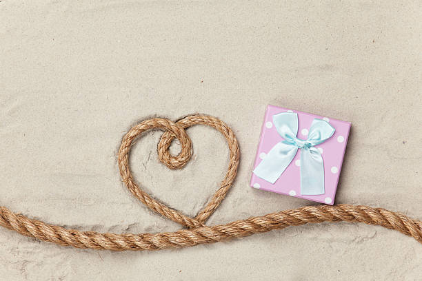 Gift box and rope in heart shape on sand background.